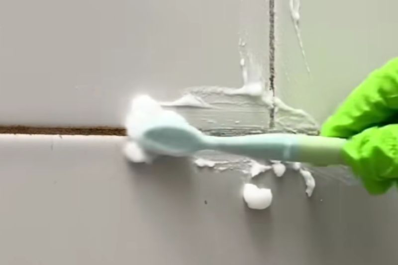 Best Ways to Clean Shower Grout (5 Proven Methods) Close-up of applying thick white baking soda paste to shower grout lines using an old toothbrush