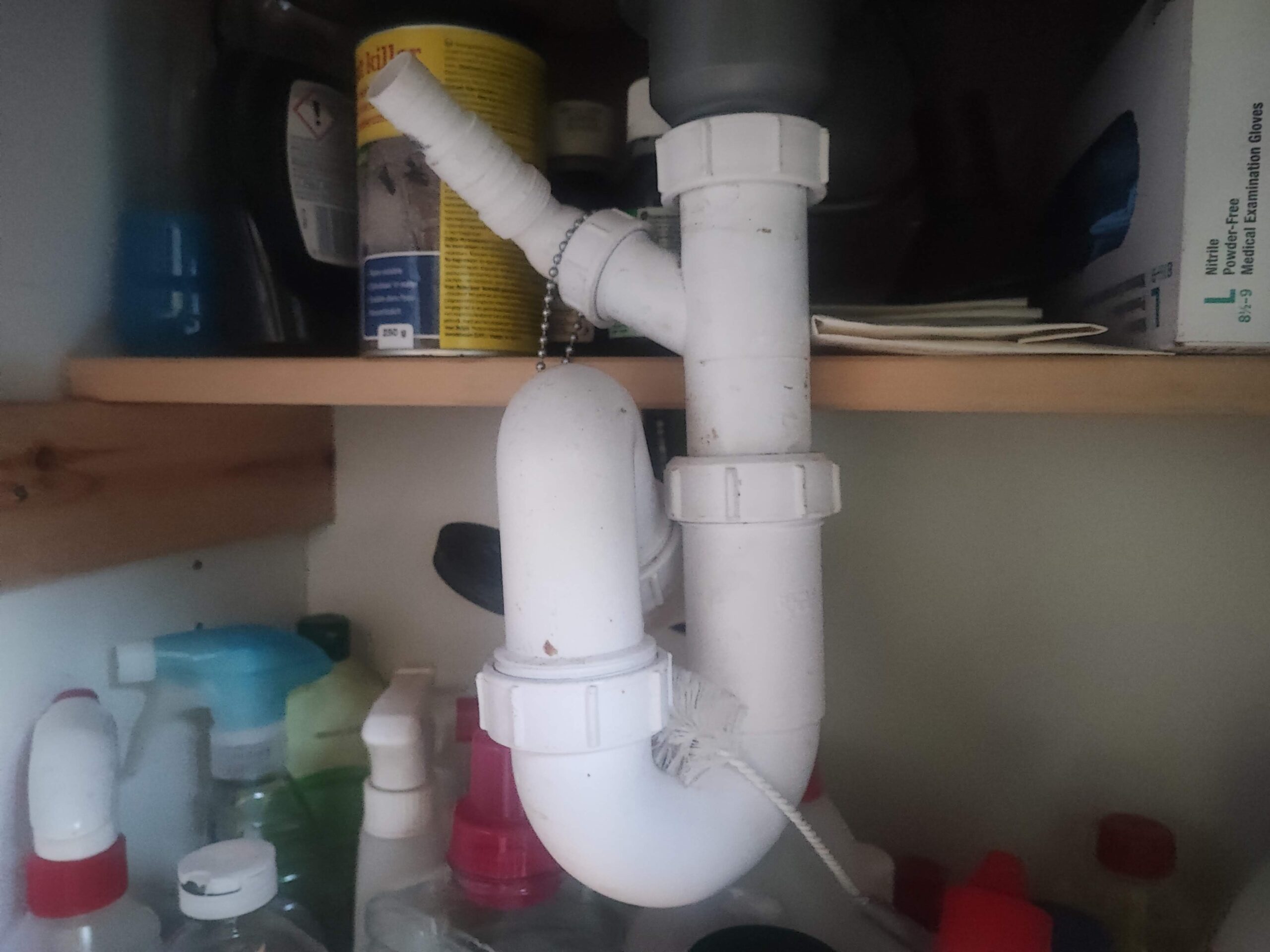 How to Clean a Kitchen Sink Drain Perfectly P-trap pipes under a kitchen sink with a bucket placed underneath to catch water during cleaning