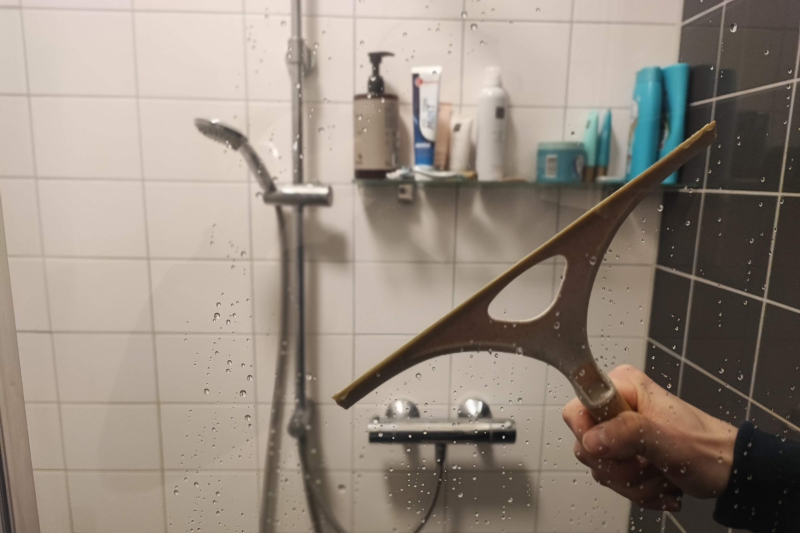 Best Ways to Clean Shower Grout (5 Proven Methods) Squeegee hanging on shower glass door with clean bright shower visible in background