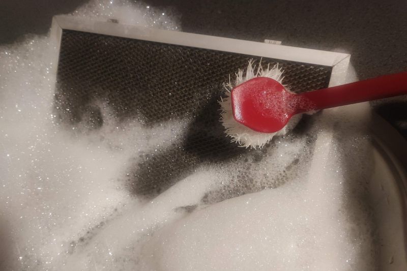 How to Clean a Range Hood Filter (Degrease in Minutes) Scrubbing a range hood filter with a brush under running water to remove grease