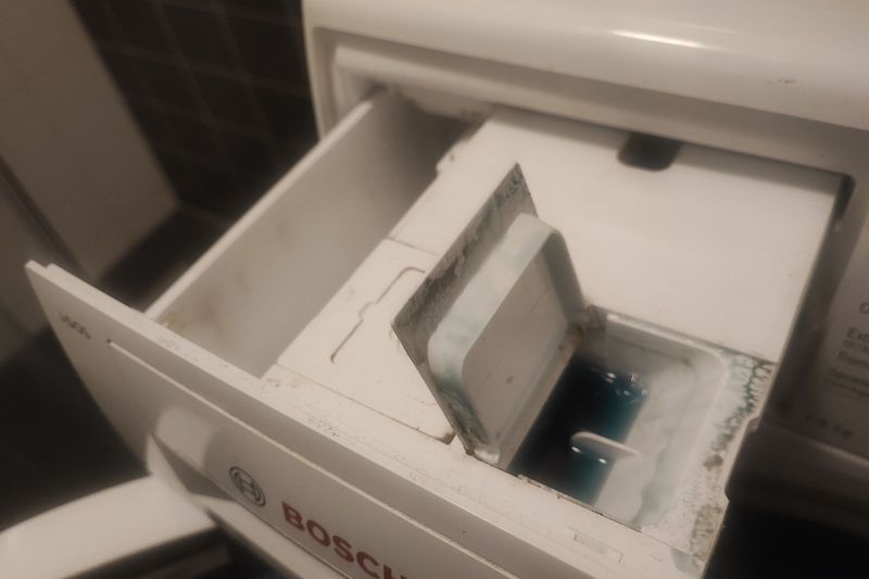 How to Clean a Front Load Washing Machine Step by Step Pulled-out detergent dispenser showing visible buildup of congealed detergent and fabric softener