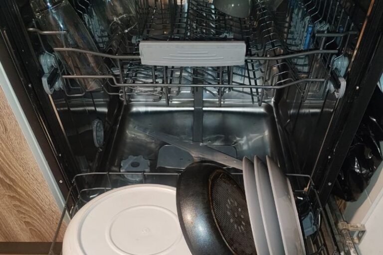 How to Clean a Dishwasher (Filter, Spray Arms & More) Open dishwasher with neatly loaded dishes, including a frying pan and plates on the lower rack. The stainless interior is clean and shiny.