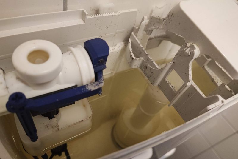 How to Clean a Toilet Tank (Step-by-Step Guide) Open toilet tank lid revealing sediment, mineral buildup, and discoloration inside the tank