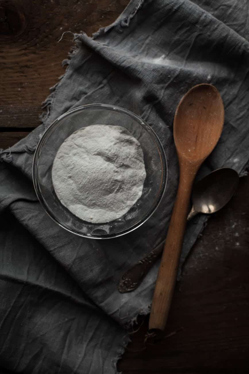 How to Remove Water Stains from Glass (Easy Methods) Close-up of hand applying thick baking soda paste to a glass surface with stubborn cloudy water stains